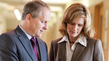 A man and woman in suits reading a document together.
