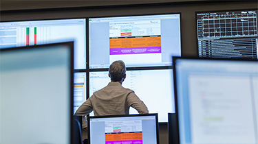 A man reading data from many large computer screens on the wall. 