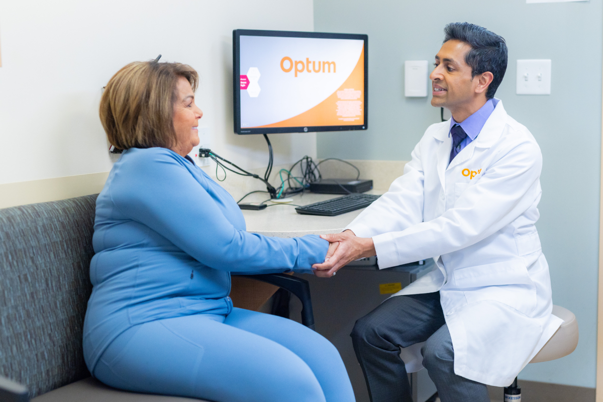 A doctor embracing a patient by holding her hands as they talk in front of a computer.
