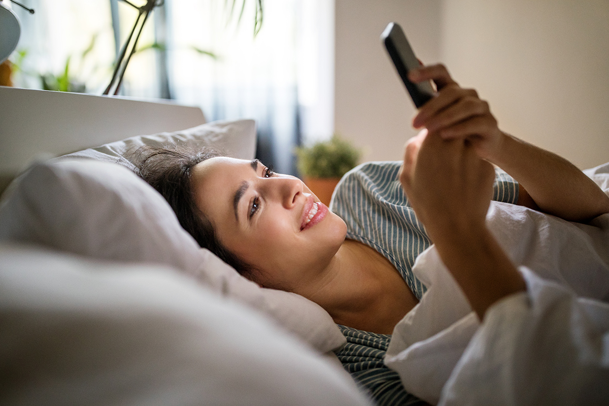 Young woman lying in bed looking up doctors on her phone