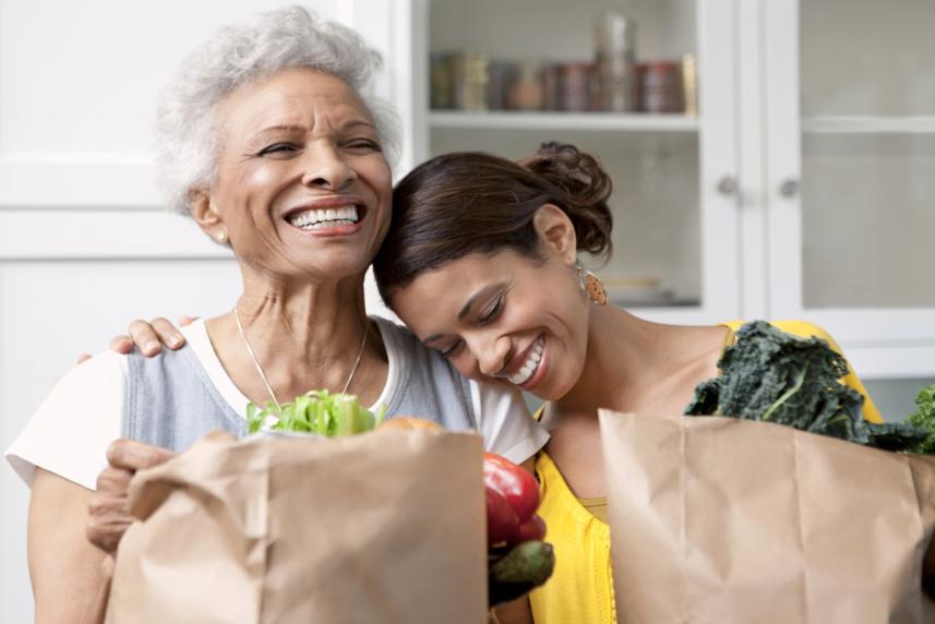 Two women smiling with each other while holding bags of groceries