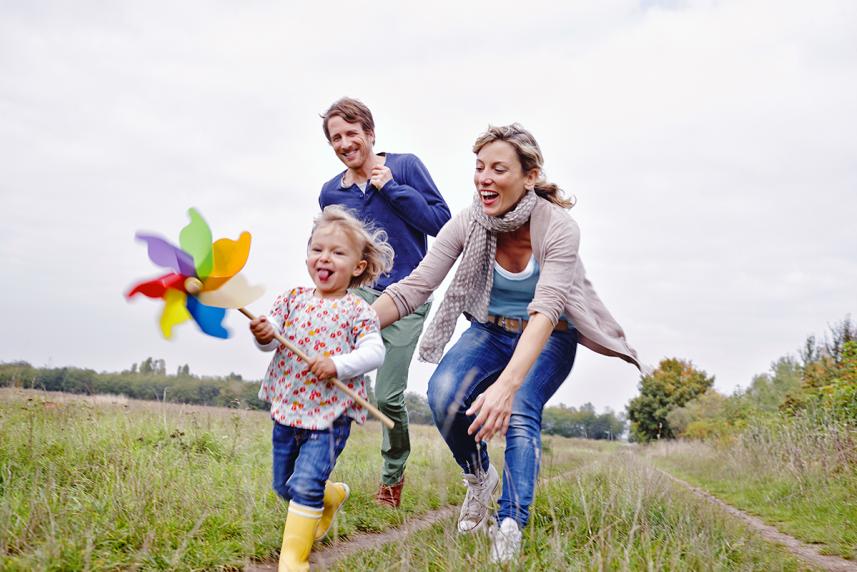 Little girl running with a pinwheel in her hands while her parents run with her