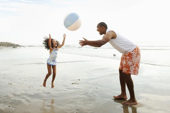 A man and a child at a beach playing with a beach ball