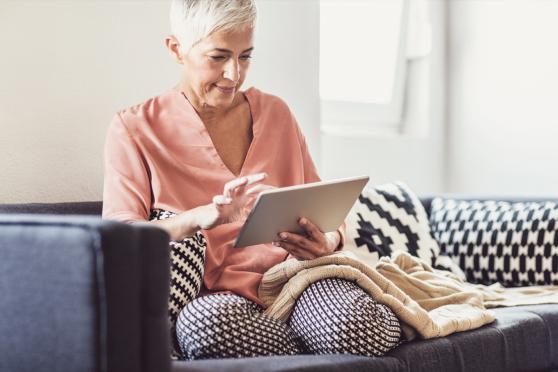 Woman on the couch looking up open enrollment information on her tablet.