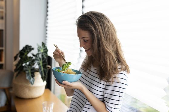 Woman eating noodles for an article about the best nutrients for hair and nails